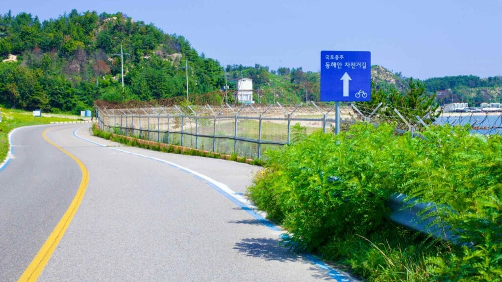 Alongside a road near the north end of Gonghyeonjin Beach, a bike path sign and a distinct blue line indicate the route as part of the Gangwon bike path.