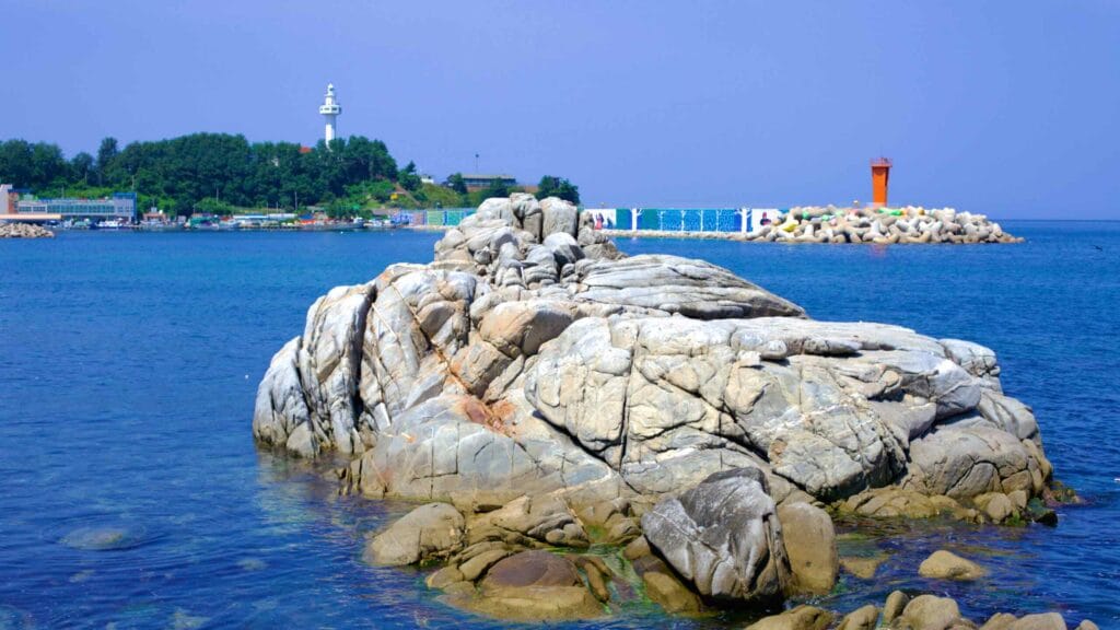 Overlooking Daejin Port, a large rock emerges from the East Sea, with Daejin Lighthouse standing guard on the hill above.