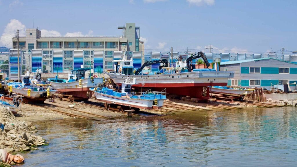 The dry dock at Geojin Port presents a scene of various boats, from small vessels to large ones, raised and out of water.