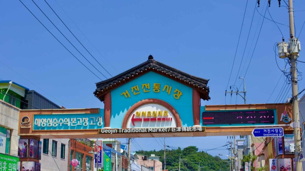 An overhead sign marks the entrance to the bustling Geojin Traditional Market along the main road through Geojin Port.
