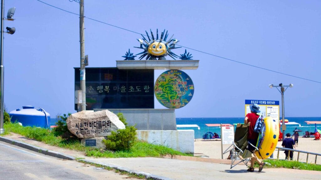 At the north end of Hwajinpo Beach, a granite sign with a sun statue directs visitors towards Chodo Port and beach.