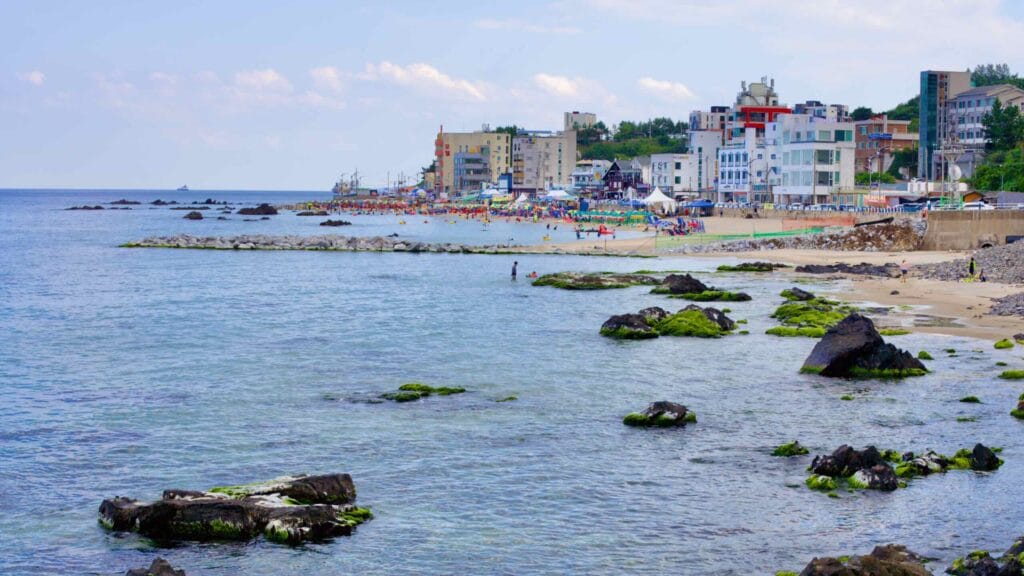 Overlooking Eodal Port and Beach, where rocks guard the sandy shores, people enjoy the water shielded by breakwaters.