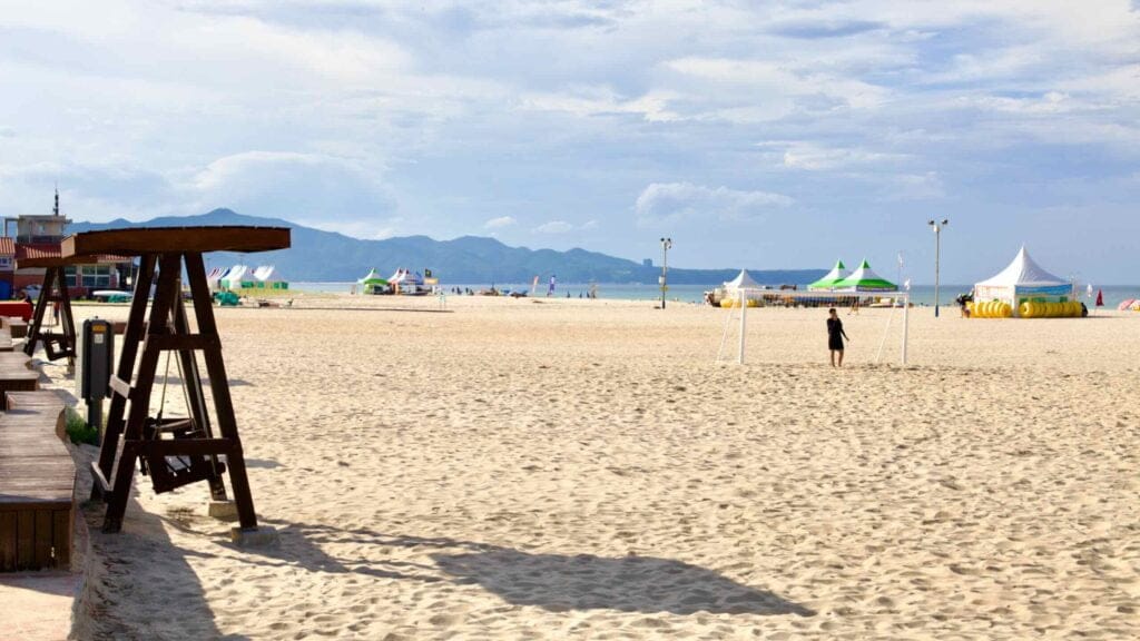A swing on the sandy shores of Mangsang Beach offers a peaceful retreat, while nearby, visitors enjoy soccer and explore tents filled with beach rental equipment on a sunny day.