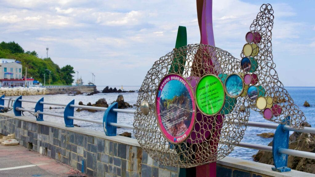 A wire sculpture of a fish along the seawall of Eodal Port serves as a poignant reminder of the environmental impact of sea pollution, urging against trash dumping on a bright sunny day.