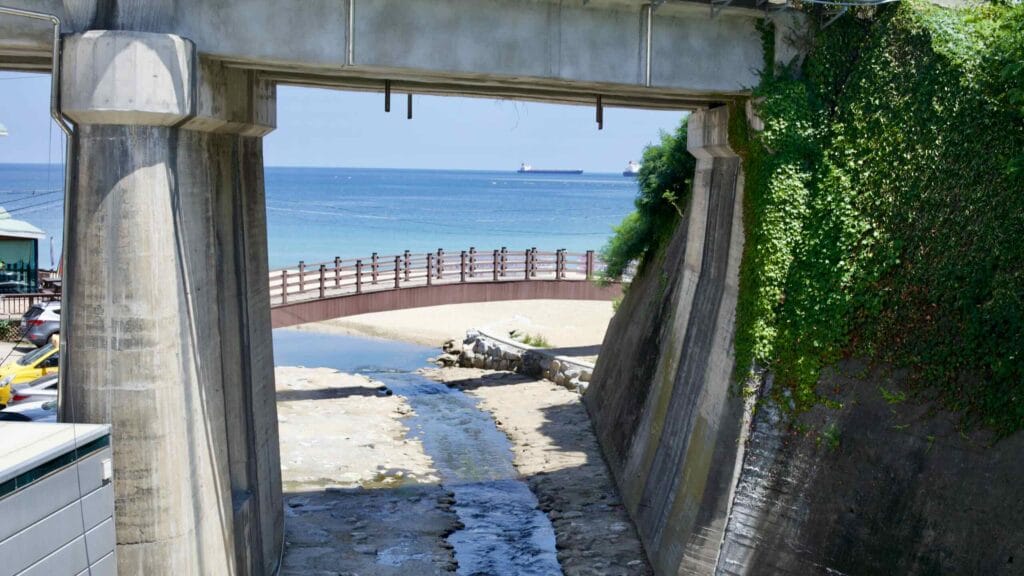 Gazing through a brick tunnel underpass, a serene stream flows from Donghae City, meandering through Hanseom Beach into the vast East Sea,.