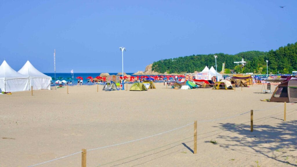 Hajodae Beach is a summer haven, dotted with large white tents and smaller family shelters against a backdrop of blue sky, golden sand, and inviting blue waters.