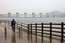 A picture of a cyclist riding through the snowy and rainy day near the Ipo Weir along the Hangang Bicycle Path.