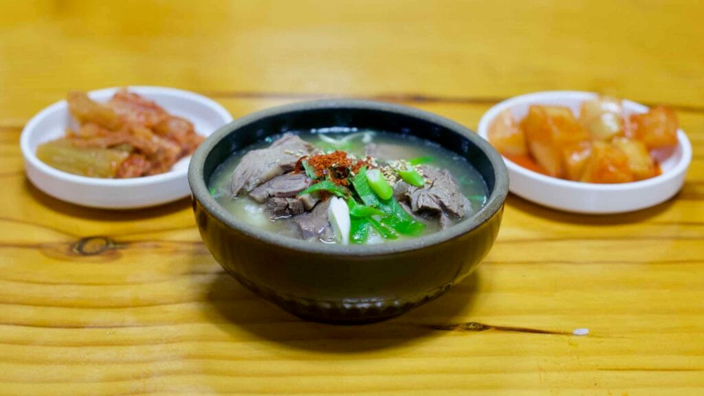 A bowl of Naju Gomtang, a traditional Korean beef soup, served with fresh green onions and red