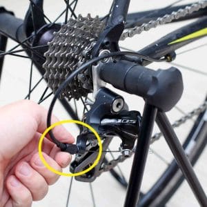 A picture of a hand turning the rear derailleur's barrel adjuster on a bicycle.
