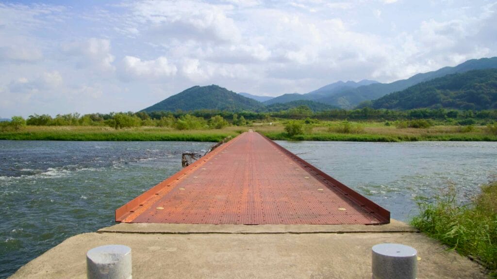 An iron bridge spans the Seomjin River, leading towards lush greenery and rolling mountains.