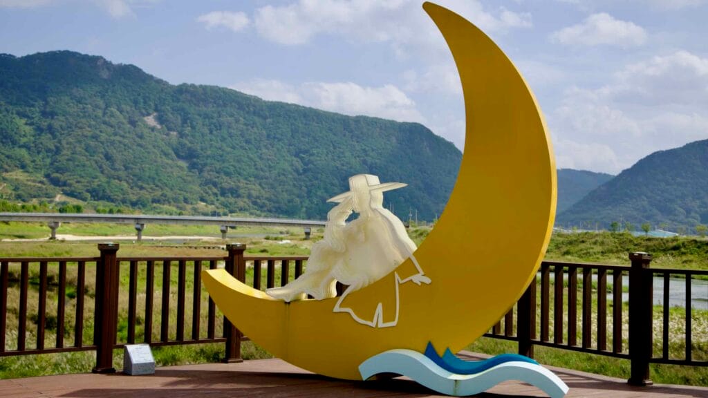 A sculpture featuring a crescent moon and a figure of a traditionally dressed Joseon-era man.