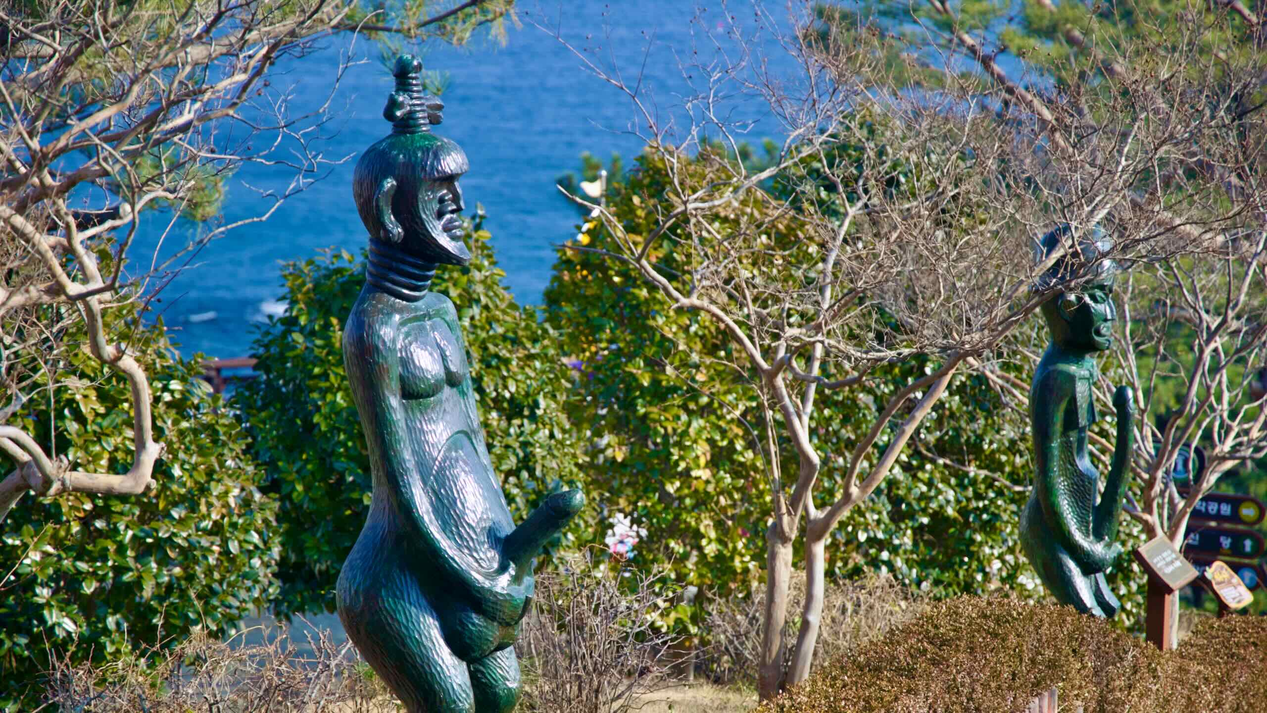 A path at Haesindang Park adorned with African-inspired statues of people and phallic figures, with the East Sea waters forming a tranquil backdrop.