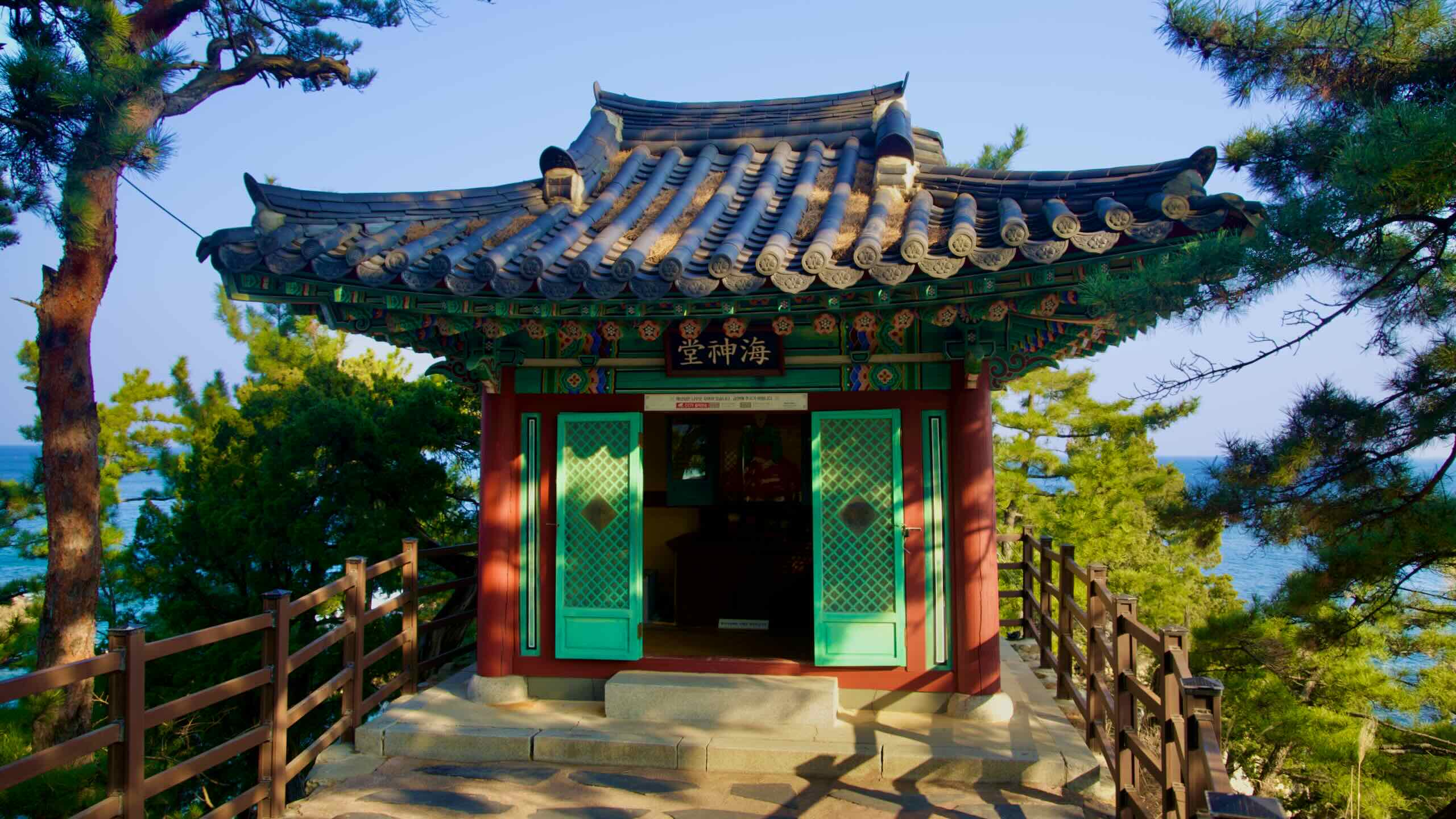 A closer view of the peaceful shrine dedicated to the lost maiden at Haesindang Park, nestled beside pine trees under a clear blue sky, with no people present.