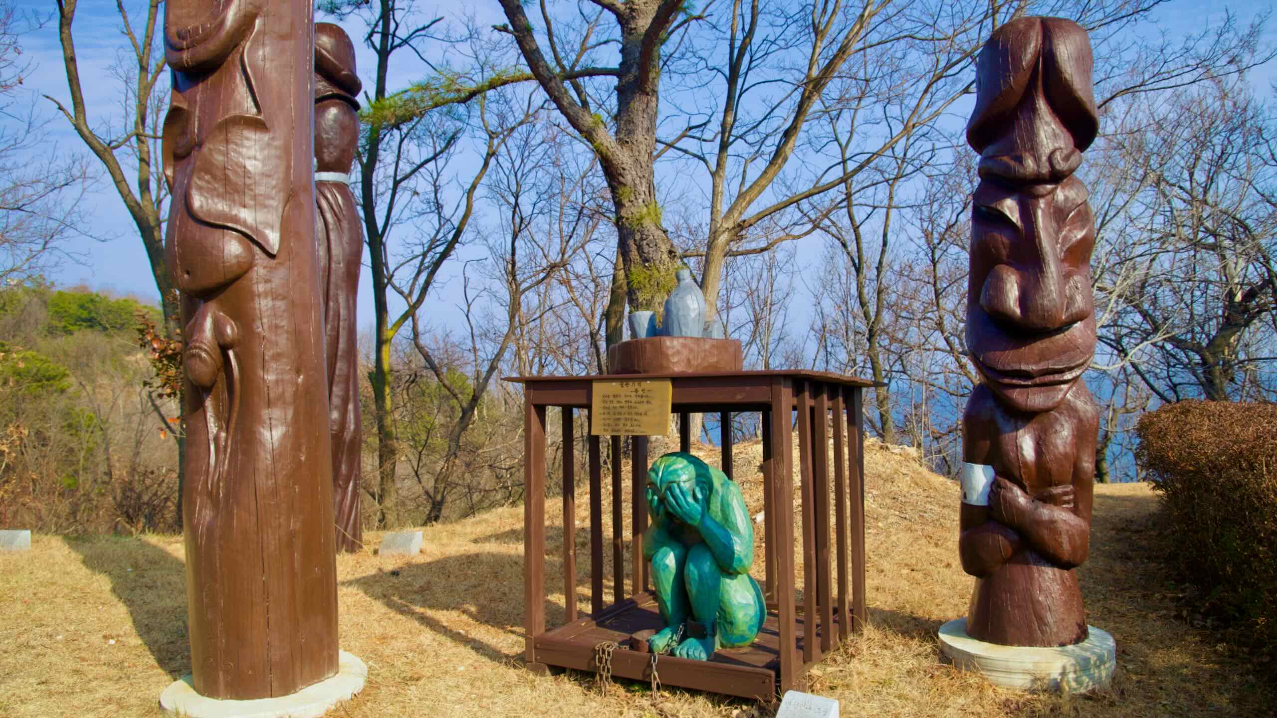 A striking array of tall wooden penis sculptures with faces, and a depiction of a woman in a cage, resonating with local folklore at Haesindang Park.