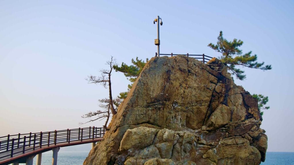 A close-up of the 20-meter tall rock observatory on the Chogok Yonggul Cave Hiking Trail, with a walking path leading up, a deck on top, the East Sea below, and the sky above.