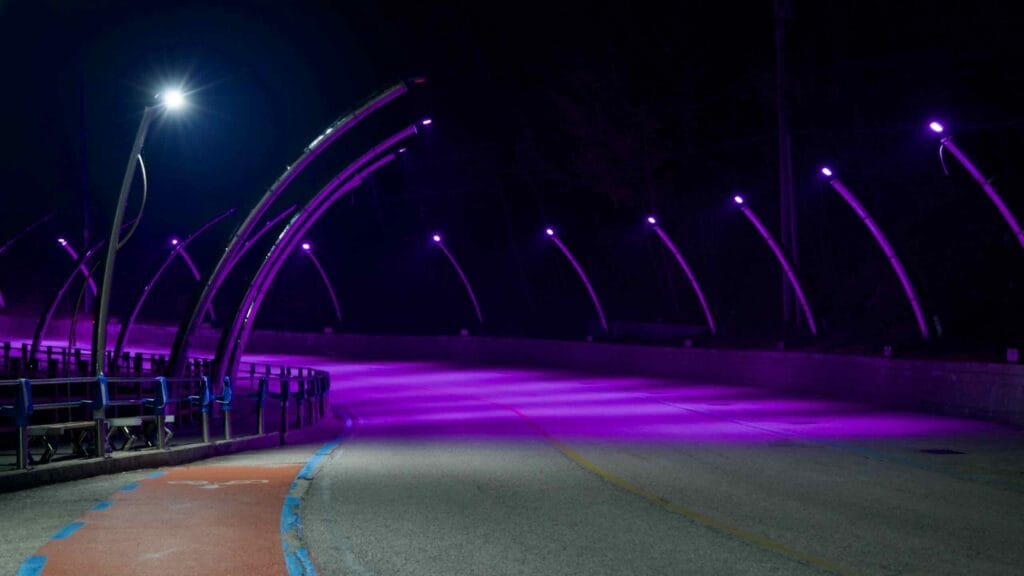 A curving hillside road at Yeongdeok Sunrise Park, illuminated in purple light by evenly spaced LED streetlights, offers a serene evening view.