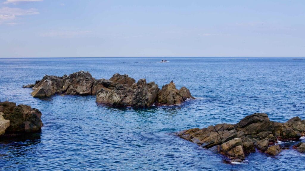 Rocks peek above the tranquil East Sea waters near Eodal Port, with the horizon stretching under a clear blue sky and blue water.