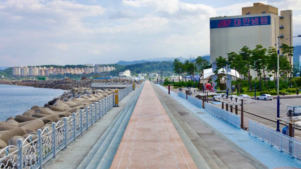 A concrete promenade and stairs lead visitors along Mukho Port, where tetrapods line the water's edge.