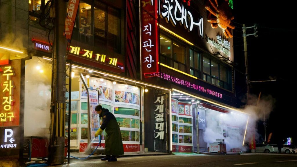 A worker sprays the storefront with a hose outside the three-story snow crab restaurant in Ganggu Port, maintaining the cleanliness and inviting appearance.
