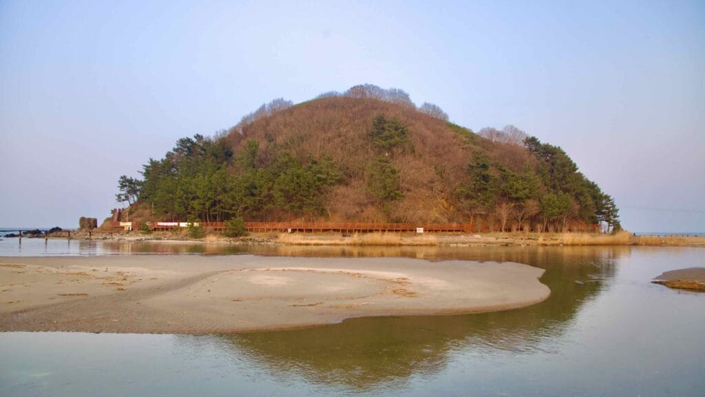 As the sun sets, stream waters near Deokbong Mountain create a serene scene, with sandbanks in the foreground and the mountain rising majestically in the midground.