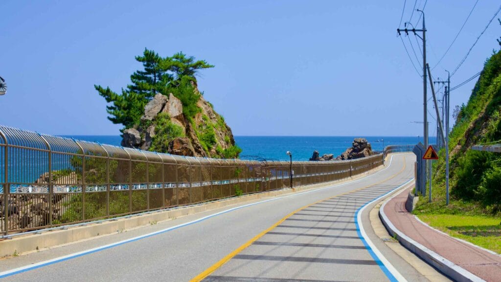 A seaside rock towering over the coastal road and a military fence near Geojin Port.