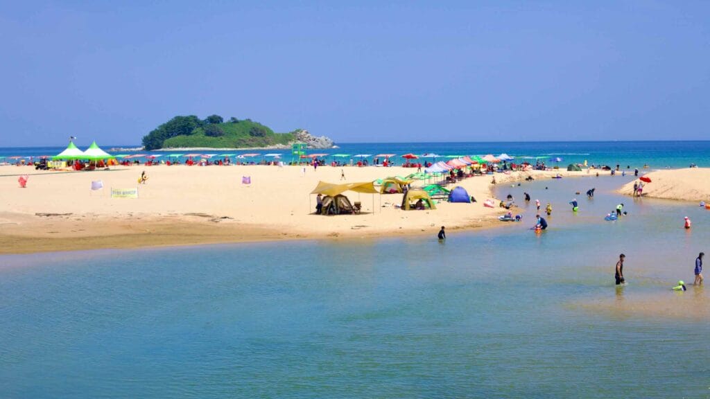 Tourists enjoy the shallow, clear waters of Hwajinpo Beach, where a freshwater stream meets the East Sea.