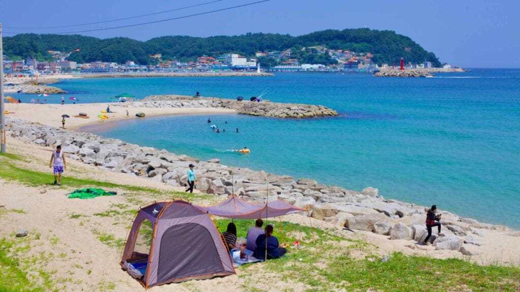 At the north end of Geojin Village Beach, rocks hug the water's edge with a small sandy breakwater