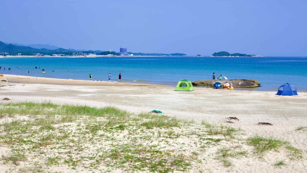 Sampo Beach unfolds its flat sandy shores into the blue waters, dotted with tents and people.