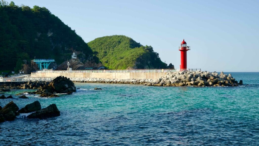 The red lighthouse at Simgok Port stands on a breakwater surrounded by concrete wave breakers.