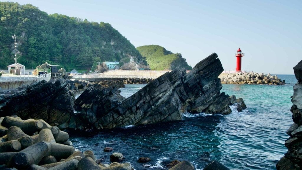 A view of the red lighthouse at Simgok Port framed by rugged coastal rocks.