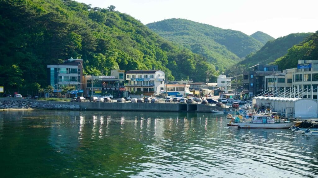 The harborfront at Simgok Port, lined with buildings and lush green hills in the background.