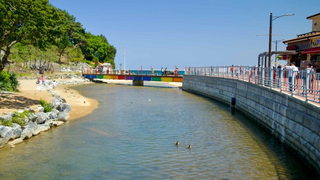 A stream flows towards Chuam Beach, with a colorful bridge and scenic surroundings near Chuam Candlestick Rock.