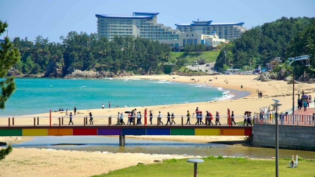 Tourists enjoy a sunny day on Chuam Beach, walking across a colorful bridge with the luxurious Sol Beach Resort.