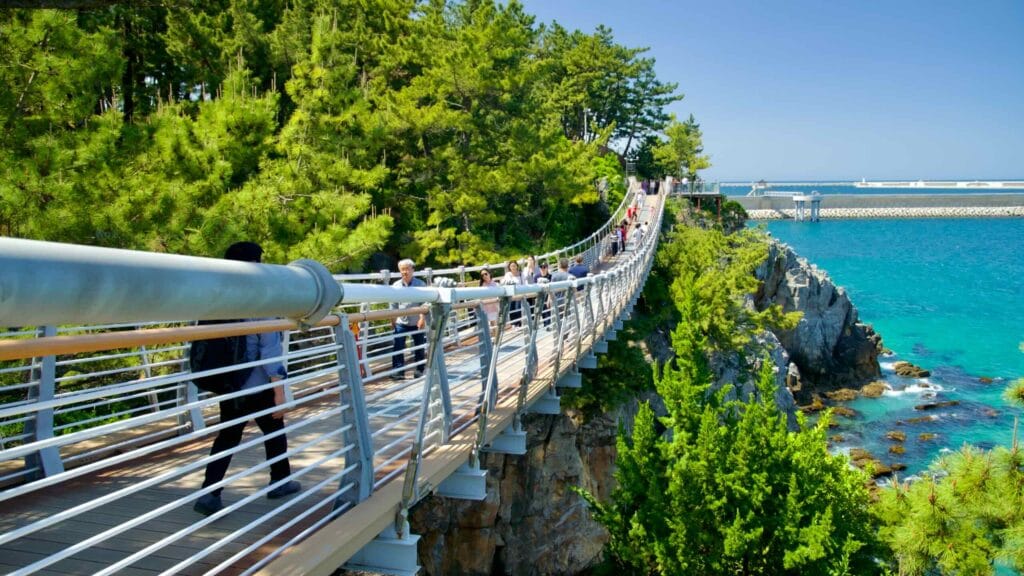 Visitors walk on the Chuam Suspension Bridge, which offers stunning views of turquoise waters.