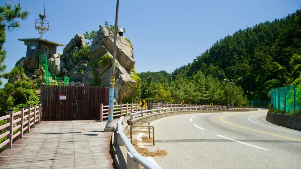 A bend in Isabu Road featuring a unique rock formation and adjacent observation area, surrounded by lush greenery and forested hills.