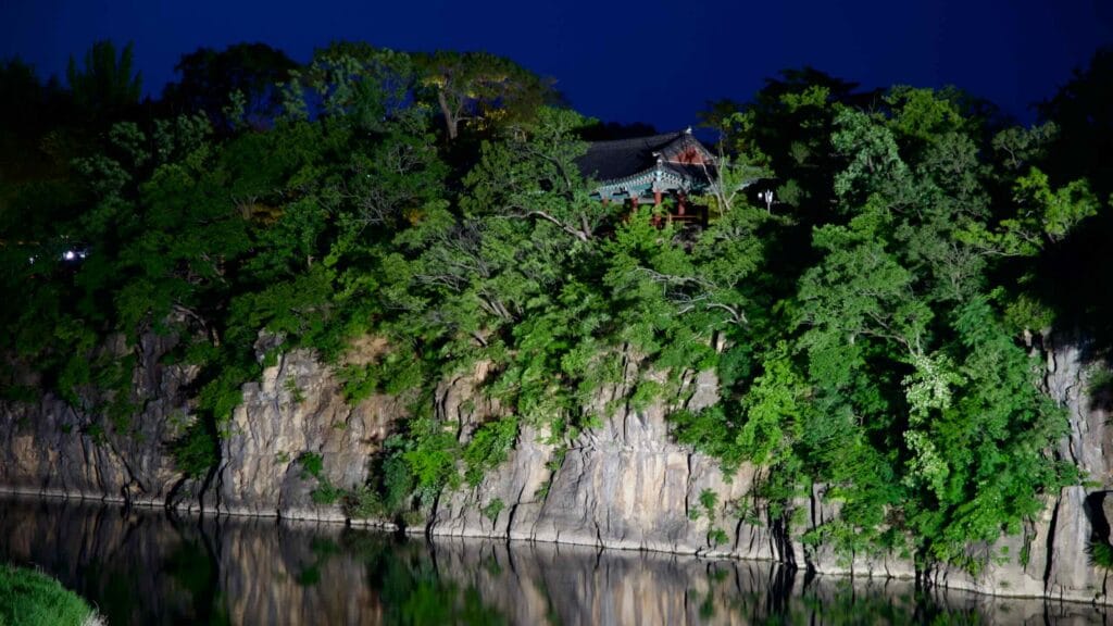 Jukseoru Pavilion illuminated at night, perched on a rocky clifftop over Osip Stream.