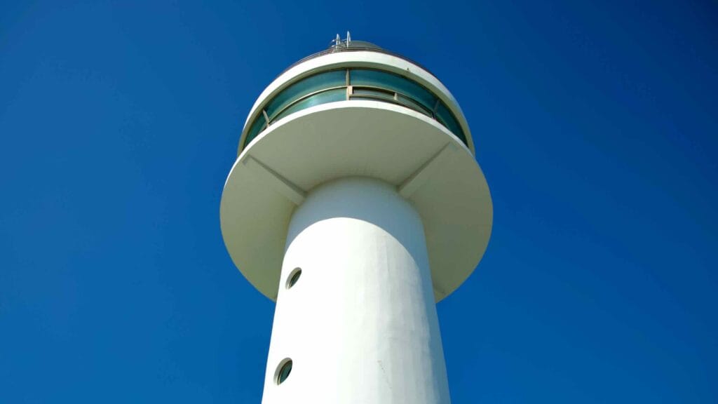 A striking view of Mukho Lighthouse, a prominent landmark perched on a hilltop above Mukho Port, standing tall under a cloudless blue sky.