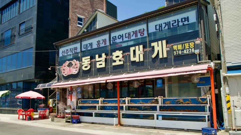 A crab restaurant at Samcheok Port featuring live crabs in tanks and outdoor seating.