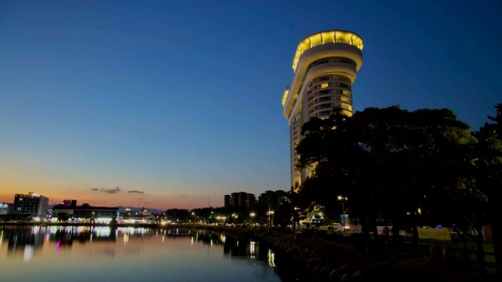 A view of the Skybay Hotel reflecting on Gyeongpodae Lake during sunset. The hotel’s lights glow against a clear evening sky, creating a peaceful scene in Gangneung.