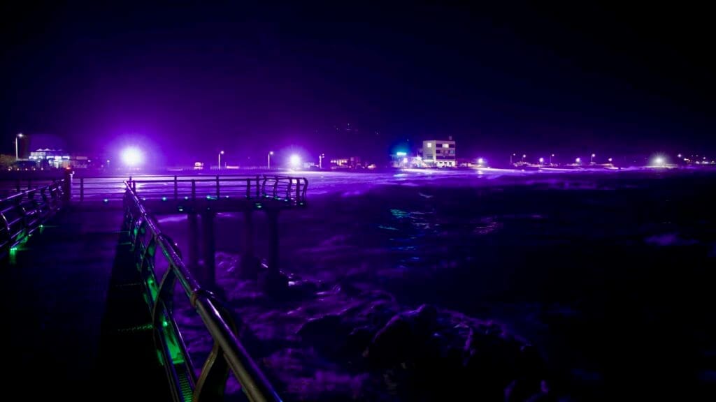 The observation walkway at Ayajin Beach casts vibrant lights over the waves.