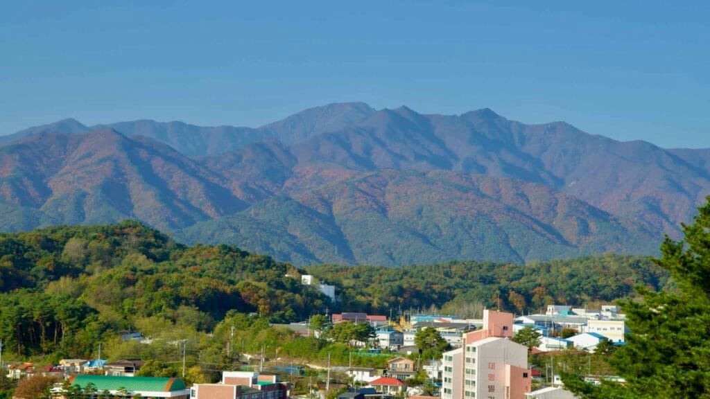 A clear view of the Seorak Mountain range as seen from Sokcho, showcasing its rugged peaks and autumn foliage with the city nestled in the foreground.