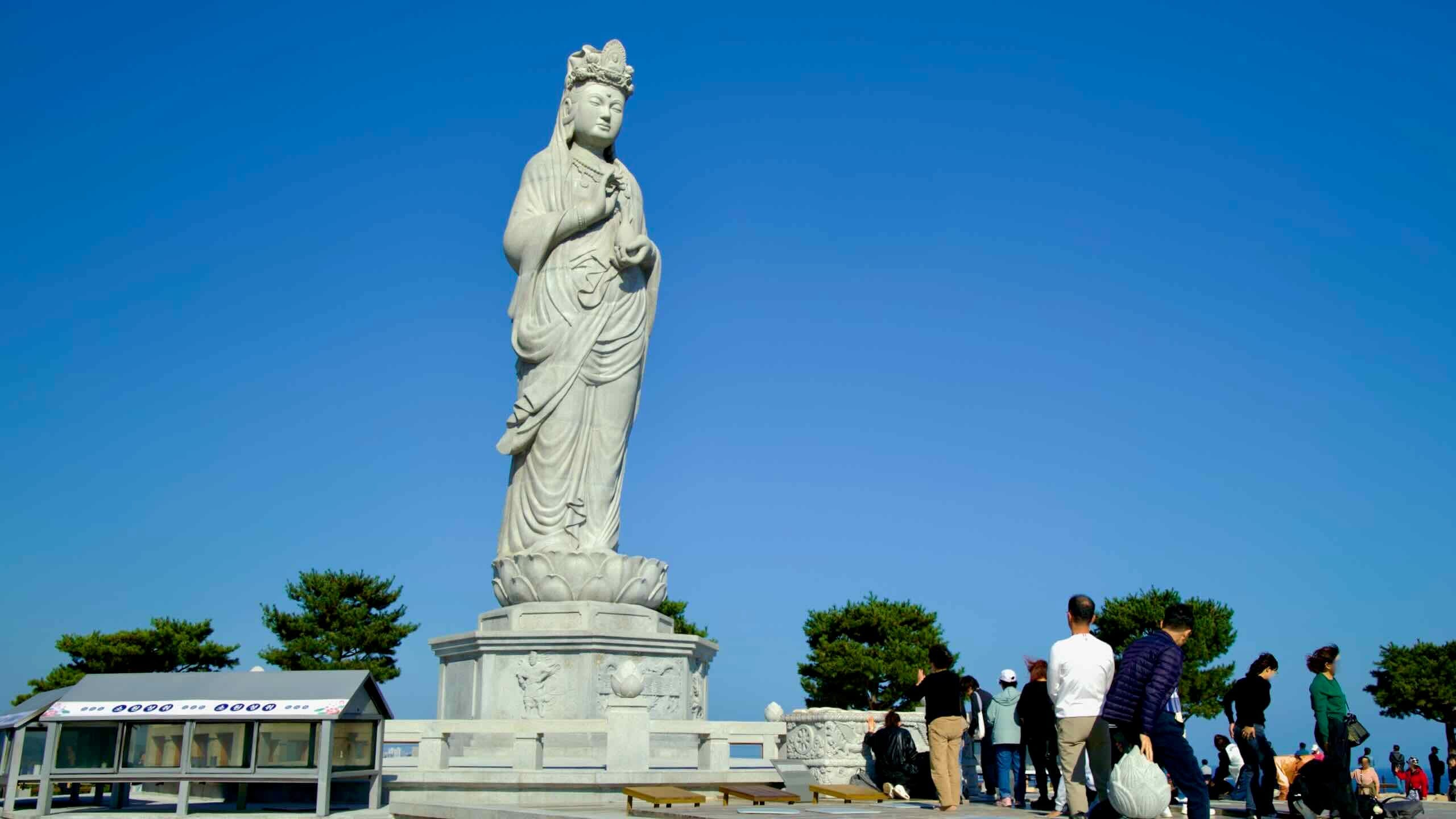The towering Seawater Avalokitesvara statue, a 15-meter-tall landmark at Naksansa Temple, stands against a clear blue sky, drawing worshipers and visitors.