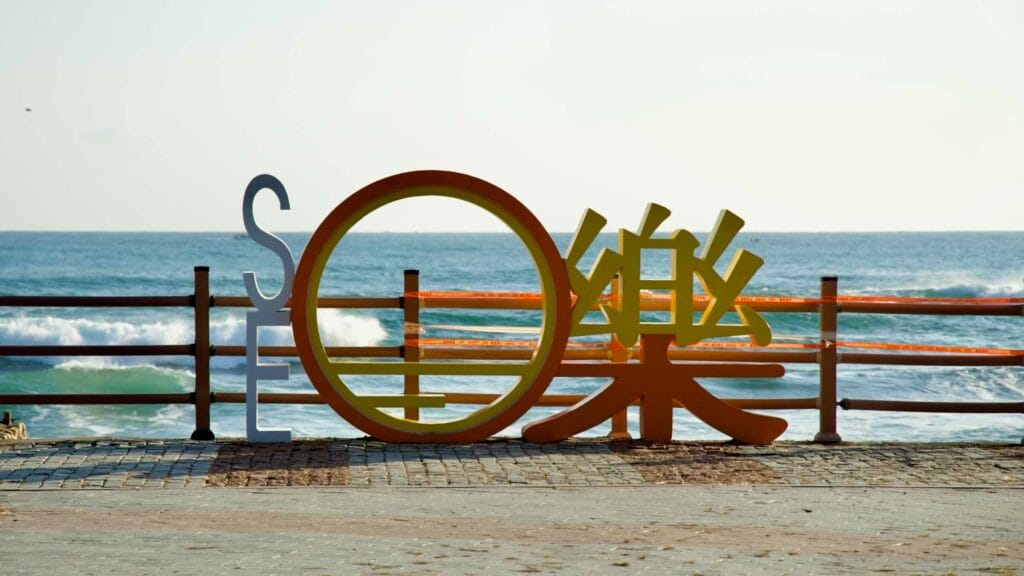 A vibrant Seorak sign installation at Seorak Sunrise Park with stylized Korean characters, set against the backdrop of the East Sea's rolling waves and scenic coastal views.