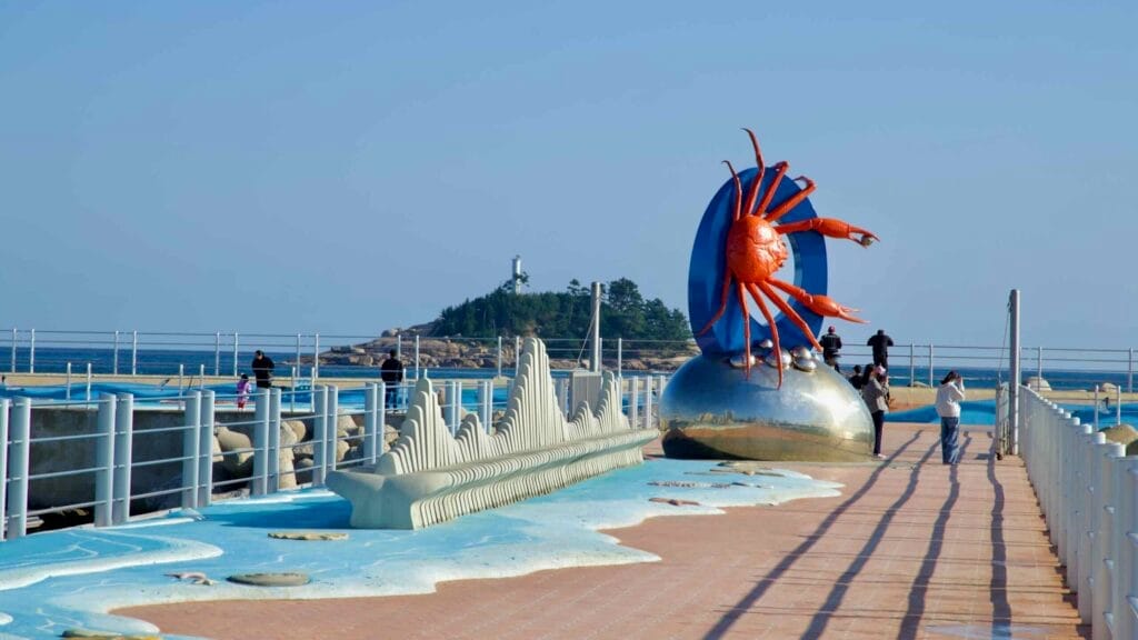 A vivid crab sculpture sits prominently on the breakwater at Sokcho Beach, with Jodo Island and the East Sea providing a picturesque backdrop for visitors.