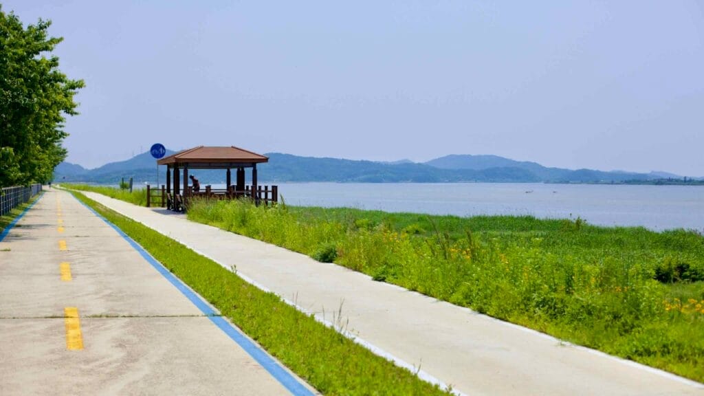 A dedicated cycling path runs parallel to the Geum River, featuring a wooden gazebo where cyclists