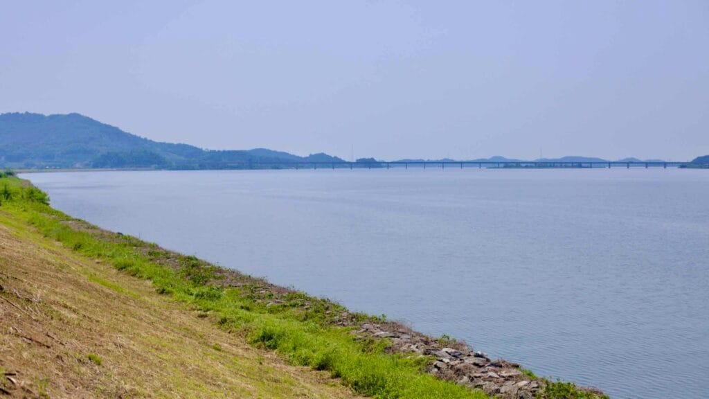A calm and expansive view of the Geum River stretches toward the horizon, with a distant bridge