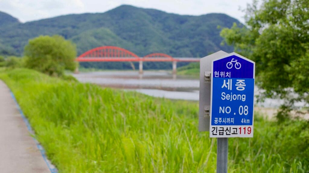 Geumgang Bike Path marker points to Gongju, with the Bulti Bridge visible over the Geum River.