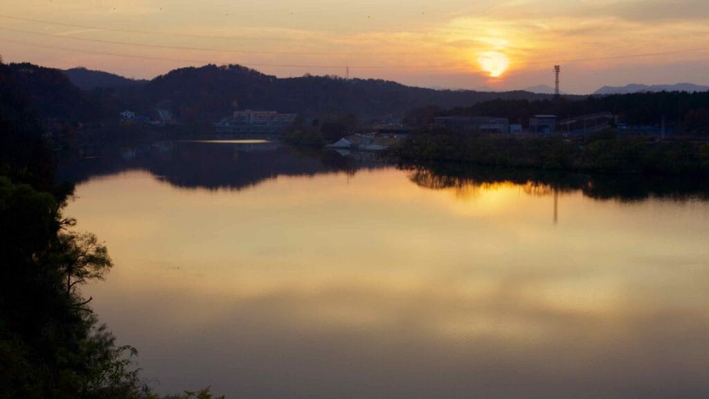 The setting sun casts a golden glow over the calm waters of the Geum River in Daedeok District.