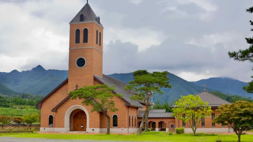 The red-brick Yeonpung Holy Land Cathedral stands against the lush Sobaek Mountains, commemorating the Catholic martyrs who sought refuge in this remote sanctuary.