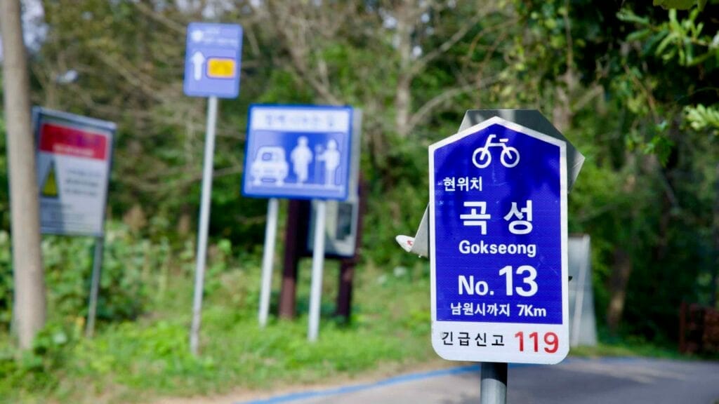 Blue cycling route sign (No. 13) on the Seomjingang Bike Path, indicating 7 km to Namwon.